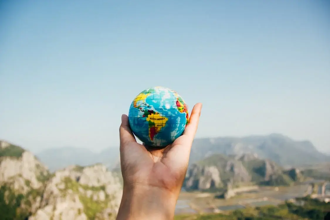 Globe being held in front of a mountain landscape